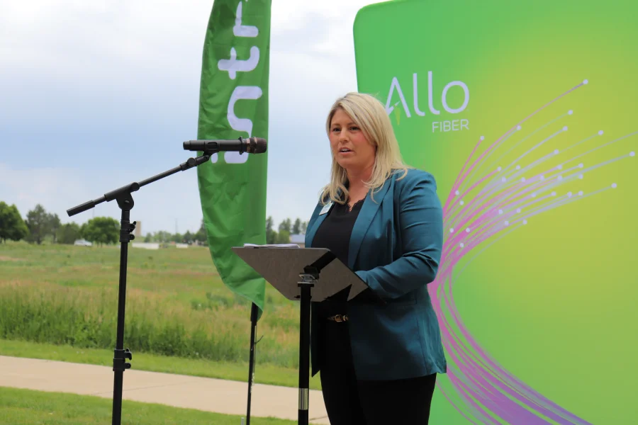 Mayor Tracie Crites speaking at an outdoor podium in front of an Allo Fiber backdrop and Intrepid flag, announcing the broadband expansion for the Town of Frederick.